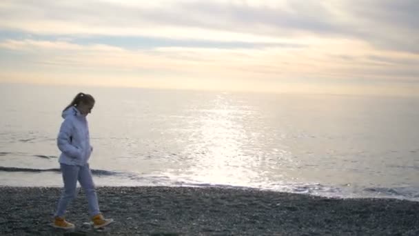 Blond kvinna med långt hår går i vit jacka nära havet havet — Stockvideo