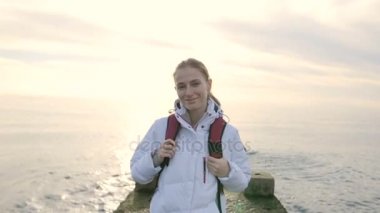 Rıhtımda sırt çantası ile deniz bir arka plan üzerinde ceketle güzel genç gülümseyen kadın portresi