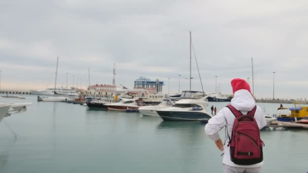 Joven hermosa chica caucásica de pie en un muelle con barcos y habla con el teléfono móvil — Vídeos de Stock