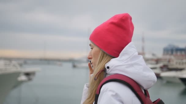 Joven hermosa chica caucásica de pie en un muelle con barcos y habla con el teléfono móvil — Vídeos de Stock