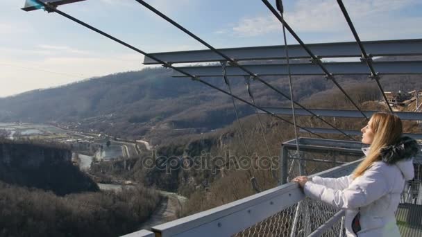 Construction d'un pont piétonnier aérien au-dessus de l'abîme, pont d'observation de la passerelle. Femme enjoing soleil et vue sur le paysage — Video