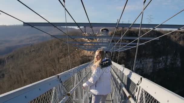 Mujer caminar a través de puente alto sobre el cañón y el gesto sígueme — Vídeo de stock