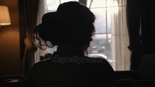 Σιλουέτα της γυναίκας μοντέλο που κάθεται μπροστά από το παράθυρο και γυρίζει το κεφάλι σε αργή κίνηση — Αρχείο Βίντεο