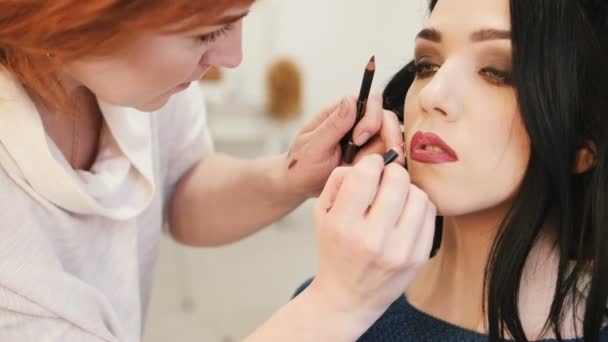 Maquillaje artista hace maquillaje labios de mujer joven con lápiz labial para acariciar los labios — Vídeo de stock