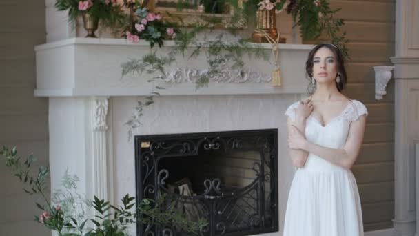 Hermosa novia morena juguetona con vestido blanco posando en el fondo de la chimenea — Vídeos de Stock