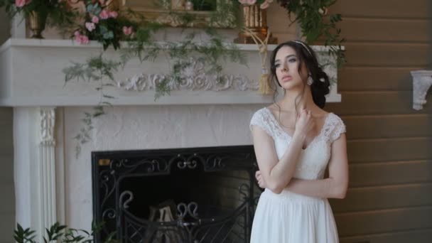 Hermosa novia morena juguetona con vestido blanco posando en el fondo de la chimenea — Vídeos de Stock
