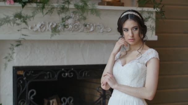 Невеста в белом платье сидит дома и позирует фотографу — стоковое видео