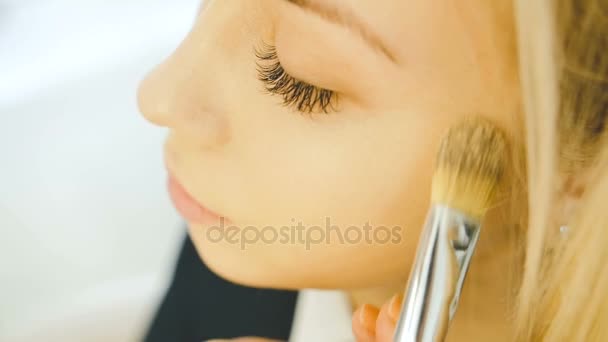 Close up shot of professional make-up artist applying Makeup on the face of the beautiful young sensual model with blonde long hair. Conceito de beleza e moda — Vídeo de Stock