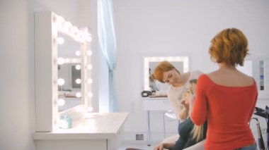 Makyöz ve Kuaför gelecekteki studio salon ayna önünde çekim için sarışın model hazırlama yan görünüm.