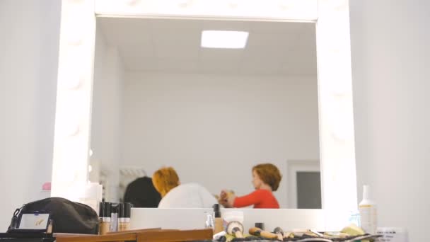 Reflexão do espelho do maquiador e cabeleireiro preparando modelo loira no salão de estúdio em câmera lenta — Vídeo de Stock
