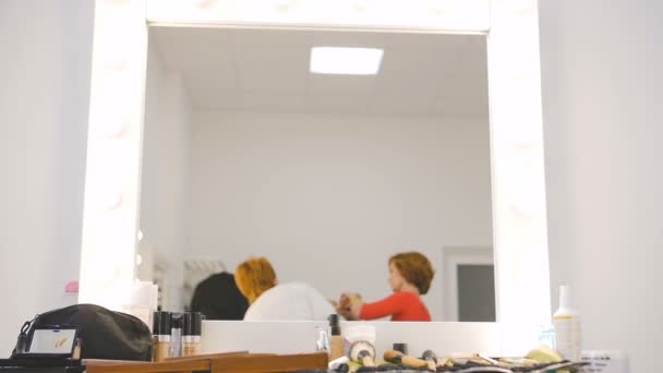 Mirror reflection of the makeup artist and hairdresser preparing blonde model at the studio salon in slow motion — Stock Video