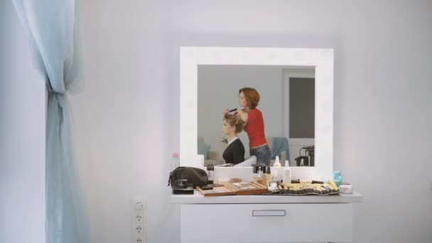 Vrouwelijke Kapper van luxe beauty salon is permanent en werken met jonge blonde model. Bekijken via de spiegel reflectie. — Stockvideo