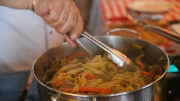 Jefe cocinar verduras fritas, espaguetis y carne en la sartén — Vídeo de stock