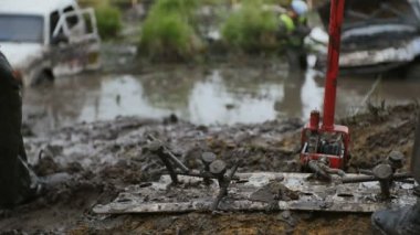 Adam işçi ağır çekimde parça jack kullanırken büyük çivi çekiç ile grev. Çamur ve toprak şaşırıp kalmış araba almaya çalışın.