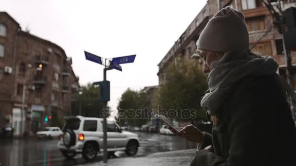 Mladá žena používající mobilní telefon na ulici na deštivý večer ve městě — Stock video