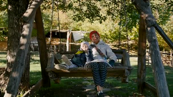 Oma und Kind fahren morgens auf der Holzschaukel im Park im Freien. — Stockvideo