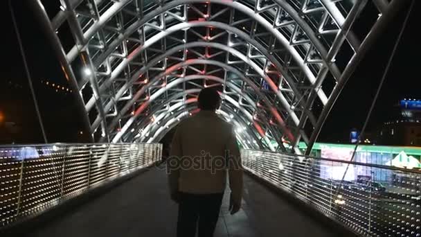 Un hombre camina sobre el puente de luces ulluminantes en cámara lenta — Vídeos de Stock