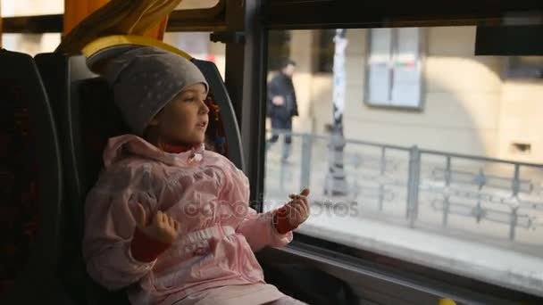 Niña rubia con una chaqueta rosa, Kid está sentado en una cabina de autobús. Sentada en su asiento y mirando a través de la ventana de vidrio . — Vídeos de Stock