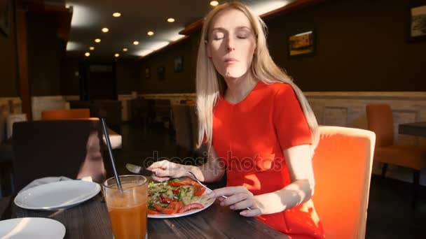 Mujer vestida de rojo comiendo ensalada fresca en un café — Vídeo de stock