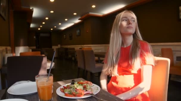 Mulher de vestido vermelho comendo salada fresca em um café — Vídeo de Stock