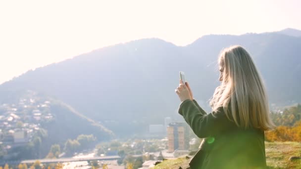 Fille prenant des photos du paysage urbain du sommet de la montagne sur téléphone intelligent cellulaire, touriste féminine debout sur la falaise Profitez du matin — Video