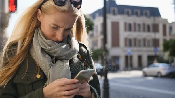 Portret van een jonge vrouw met behulp van telefoon, buitenshuis. Ernstige mooie jonge vrouw te typen op de telefoon tijdens zonnige dag. — Stockvideo