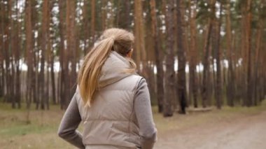 Ceketli güzel kadın 4K 'de çam ormanında tek başına yürüyor.