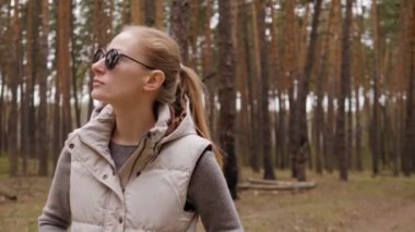 Ceketli güzel kadın 4K 'de çam ormanında tek başına yürüyor.