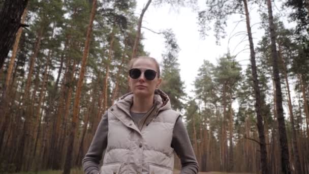 Портрет красивой молодой женщины в жилете и солнечных очках. Сосновый лес 4K — стоковое видео