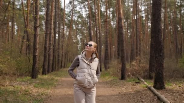 Женщина в пиджачном плаще ходит одна по тропинке в сосновом бору в 4К — стоковое видео
