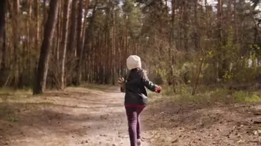 Küçük kız çam ormanında yol boyunca koşar. Deri ceket giymişti..