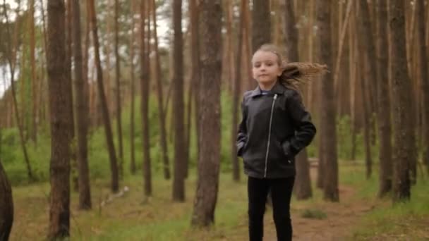 La petite fille court le long de la route du sentier dans la forêt de pins. Habillé dans la veste en cuir . — Video