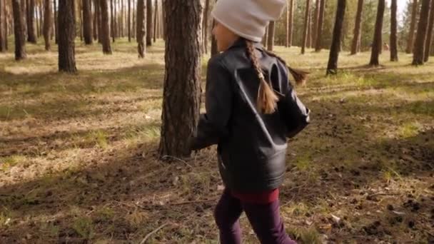 Dziewczynka biegnie ścieżką w sosnowym lesie. Ubrany w skórzaną kurtkę. — Wideo stockowe