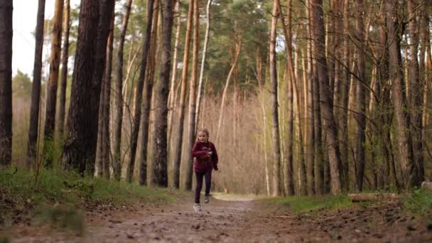 Den lilla flickan springer längs stigen i tallskogen. Klädd i skinnjacka. — Stockvideo