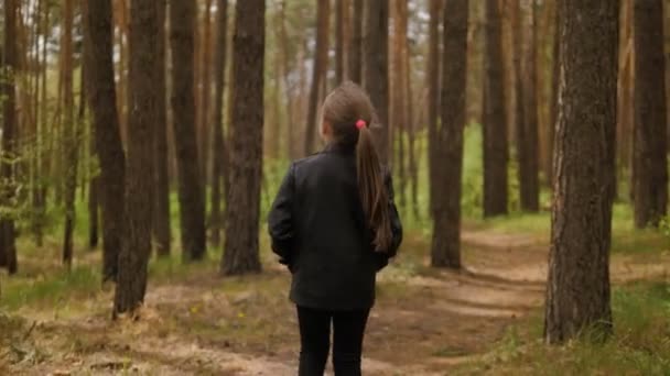 Маленька дівчинка біжить по шляху дороги в сосновому лісі. одягнені в шкіряну куртку . — стокове відео
