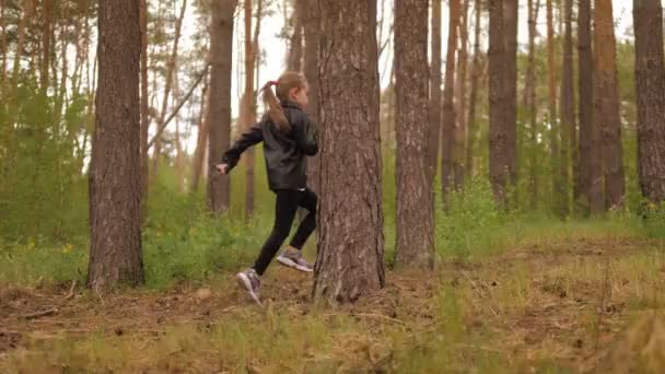 Küçük kız çam ormanında yol boyunca koşar. Deri ceket giymişti.. — Stok video