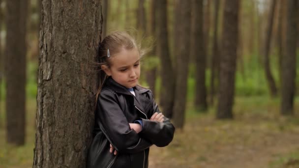 Грустная сердитая маленькая девочка, стоящая перед деревом в лесу — стоковое видео