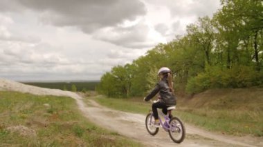 Kasklı şirin kız White Hill ve Forest arasındaki kır yolunda bisiklet sürüyor. Steadycam yavaş çekim