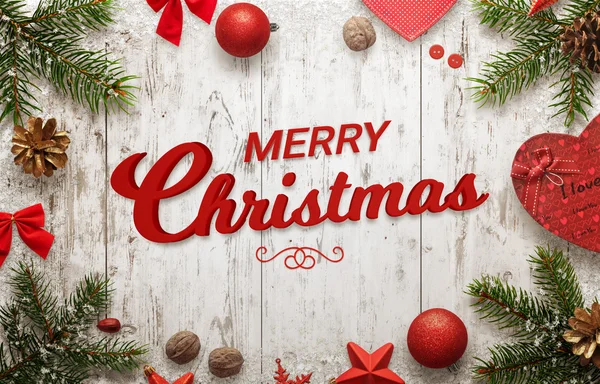 Feliz Navidad texto en la superficie de madera blanca. Árbol de Navidad, regalo, cono de pino, nuez, bolas y arcos al lado — Foto de Stock