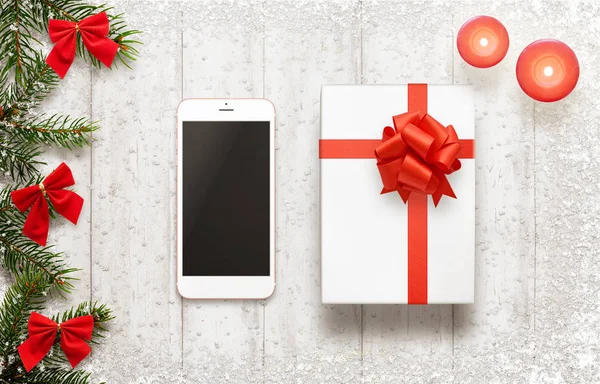Teléfono inteligente blanco y regalo de Navidad en pizarra blanca. Decoraciones de Navidad al lado — Foto de Stock