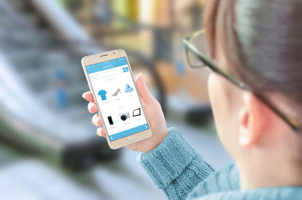 Женщина использует онлайн-приложение для покупок на смартфоне. Стекло бизнес-центра на заднем плане
.