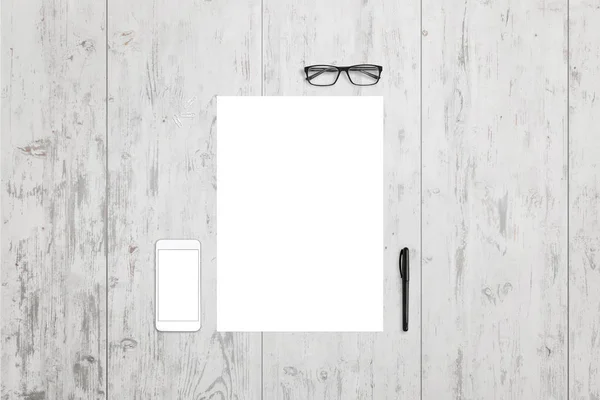 Пустая бумага и мобильный телефон на рабочем столе. Вид сверху с очками и ручкой рядом. Белый деревянный фон . — стоковое фото