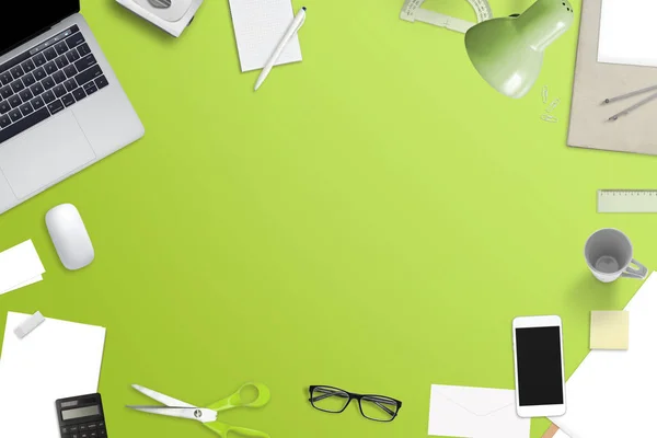 Mess on office desk with free space for text. Laptop computer, smart phone and office work accessories. Top view of green work space.