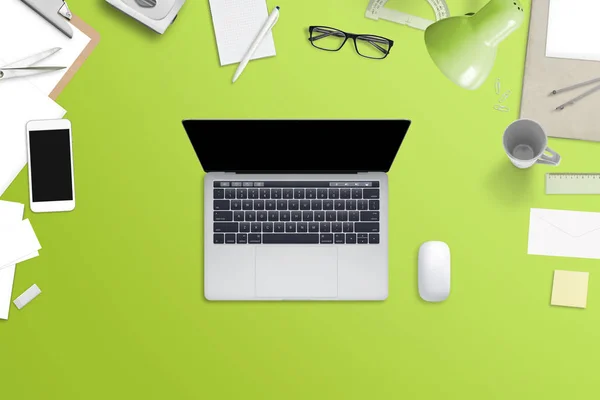 Ноутбук с чистым экраном на зеленом столе в окружении телефона, бумаги, кружки, очки, канцелярские принадлежности . — стоковое фото