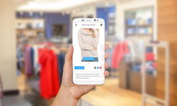 Buying sweaters and clothing online with modern mobile phone.  A weekend or holiday sales. Modern flat design app. Clothing store in background — Stock Photo, Image