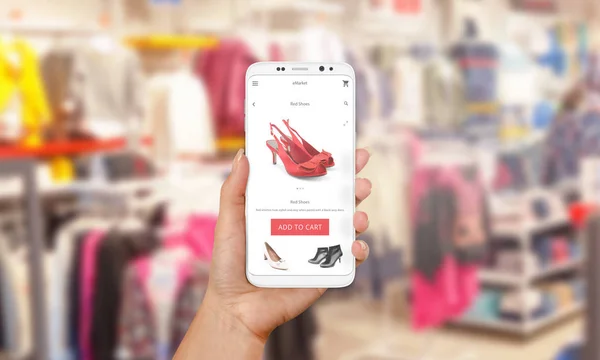 Интернет-покупки с помощью мобильного телефона. Телефон в женской руке. Магазин онлайн-приложения на экране. Магазин одежды и обуви на заднем плане — стоковое фото