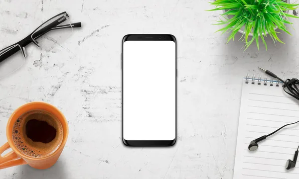 Cellulare nero sulla scrivania bianca. Schermo bianco isolato forma mockup. Display moderno con bordi arrotondati. Vista dall'alto della scrivania con caffè, bicchieri, piante — Foto Stock