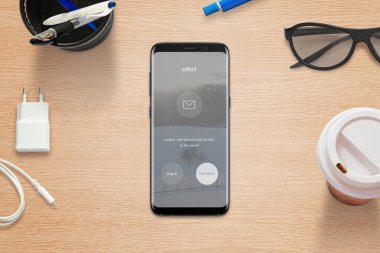 E-posta uygulaması çalışma masası üzerinde yuvarlak kenarları ile modern siyah cep telefonu. Kahve, gözlük, şarj cihazı ve kalem ile Üstten Görünüm.