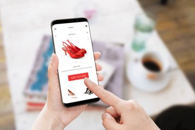 Çevrimiçi mağaza üzerinde kırmızı ayakkabılar Sepete ekle. Kadın elinde yuvarlak kenarları ile modern akıllı telefon