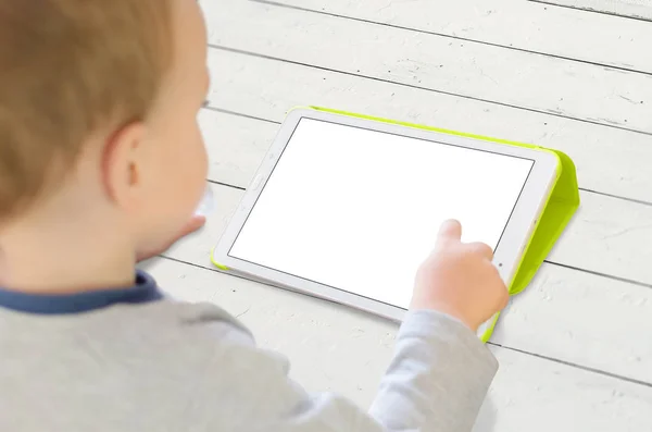 Хлопчик використовує планшет на білому дерев'яному столі. Ізольований білий, порожній екран для макету програми . — стокове фото